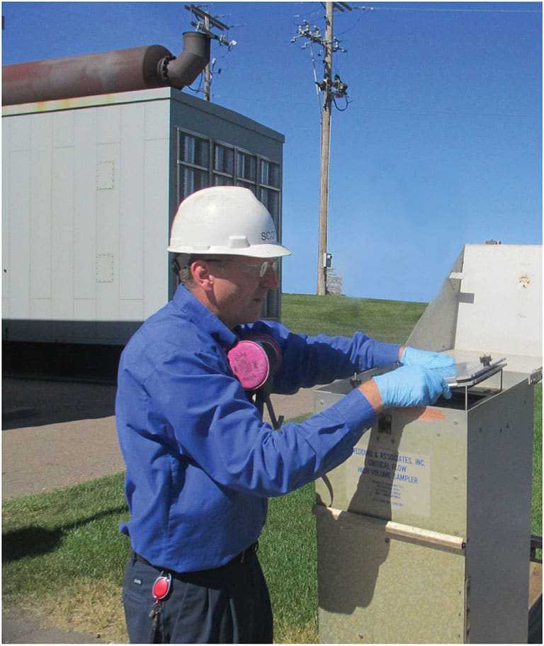 Lead battery recycling employee checking a fenceline air monitor for environmental health and safety.