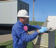 Lead battery recycling employee checking a fenceline air monitor for environmental health and safety.