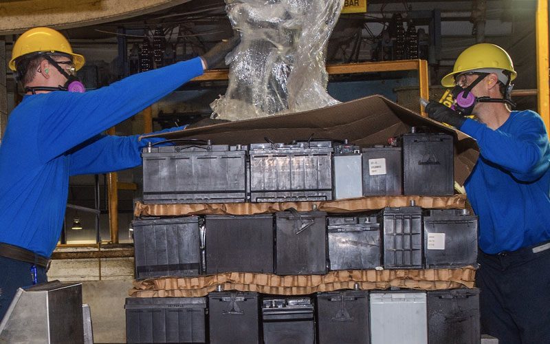 Lead battery recycling employees pulling plastic off a pallet of used lead batteries.