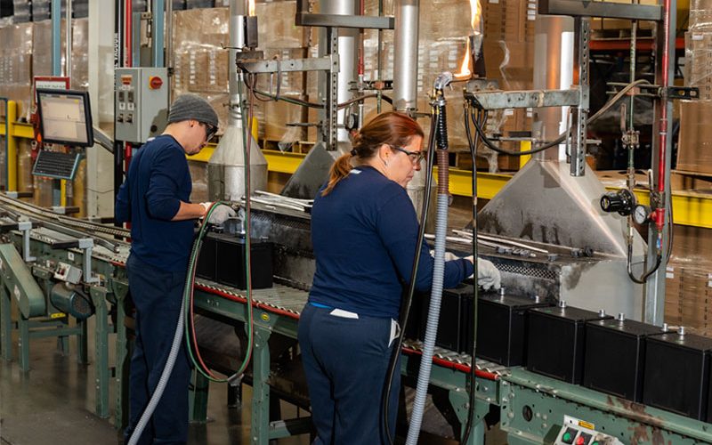 Lead battery manufacturing employees filling new lead batteries with raw materials from sustainable recycling.