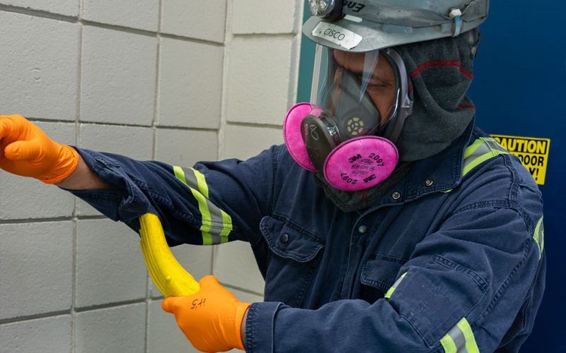 Man in PPE uniform vacuuming himself as an employee safety procedure for lead battery recycling facilities.
