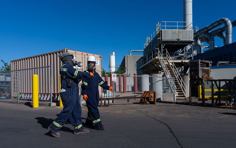 Two lead battery recycling employees in full employee health and safety PPE walking outside a recycling facility.