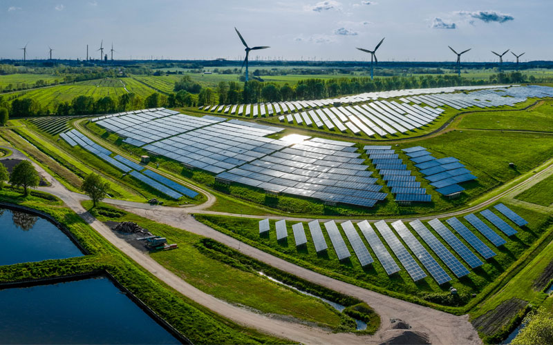 Scenic shot of green fields with solar panels and wind turbines showing renewable energy stored by lead batteries.
